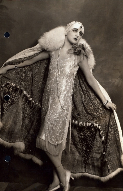 Sepia tones, person wearing a mid lenght dress with a cloak and pearl accesories.