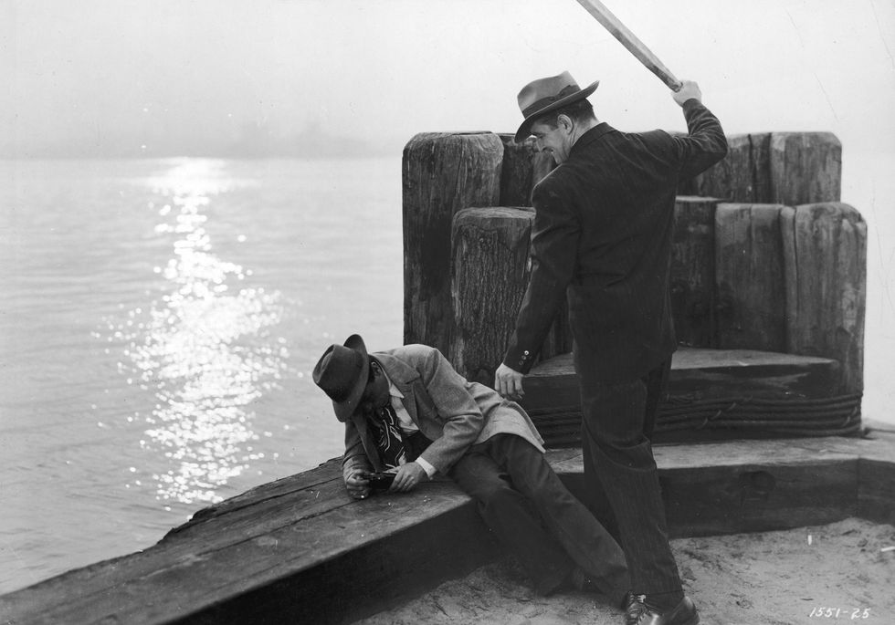 Monochrome, man getting beated by other man with a bat on a dock overlooking the sea.