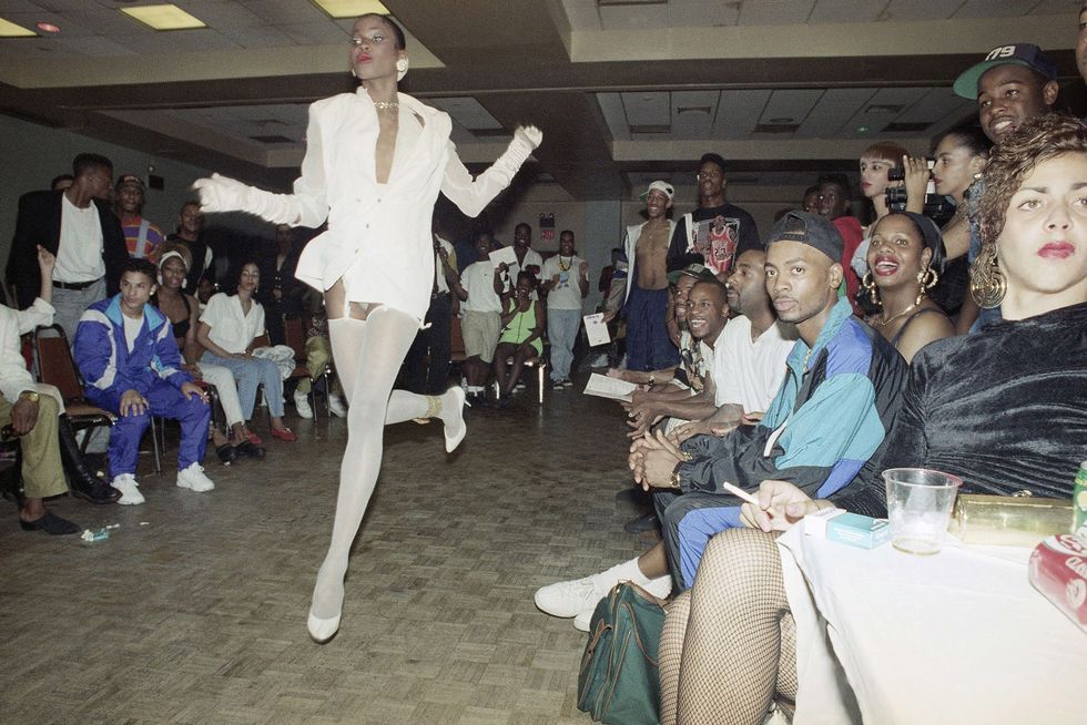 Ballroom attended primarily by black and brown people sitting and watching the performer in the runway