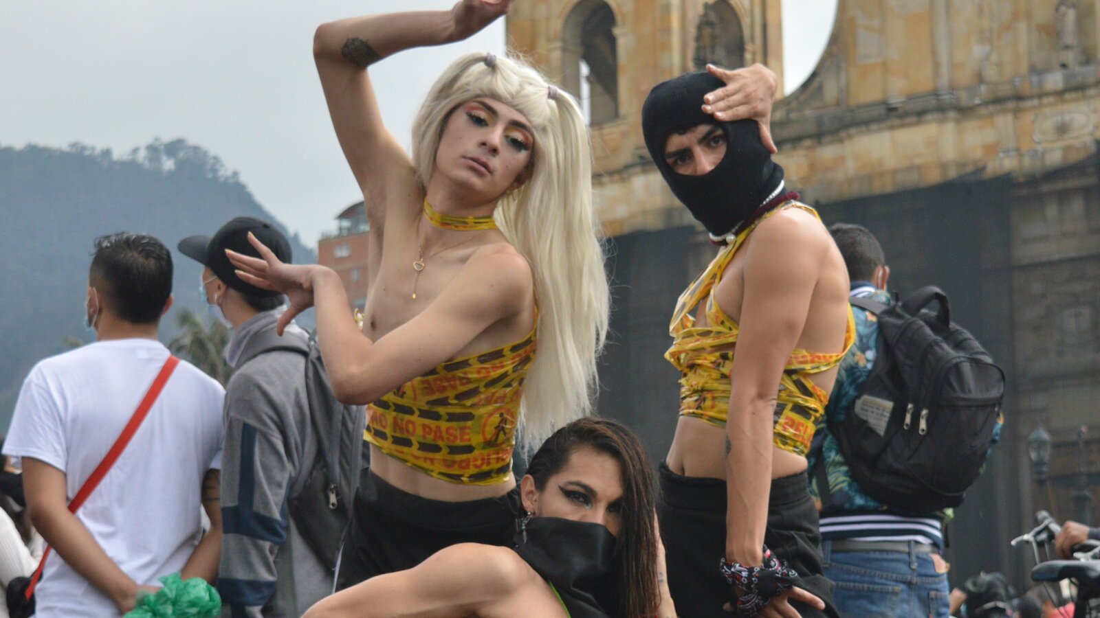 Group of 3 queer people in vogue poses at a riot.